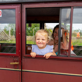 Little girl poking her head out of a train carriage, mum in background