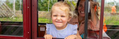 Little girl poking her head out of a train carriage, mum in background